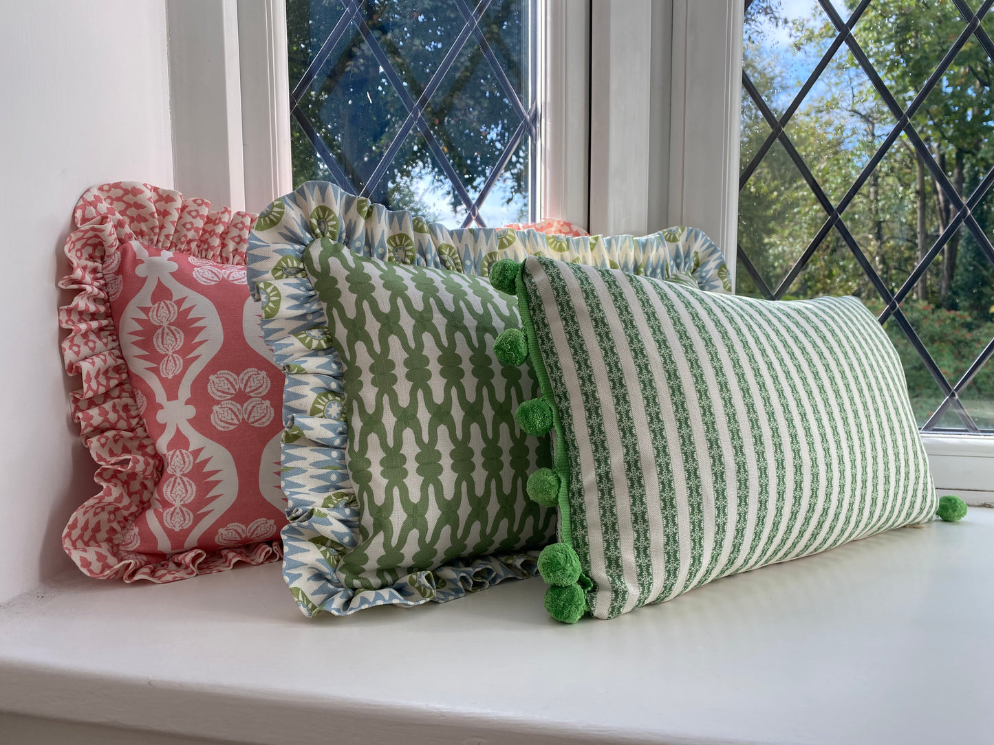 three cushions. one pink with pink frill. one is green with frill. Green striped cushion with green pompoms.