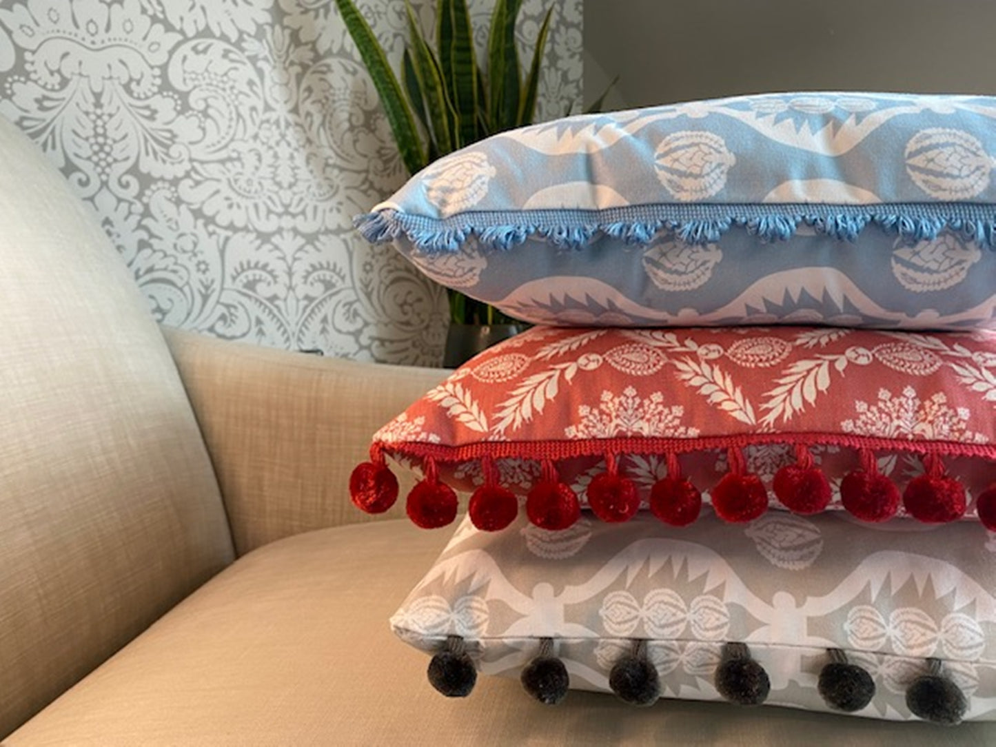 Stack of cushions Georgie fabric grey with pompom trim plus Rosie fabric red with pompom trim plus Georgie fabric blue and white with fan trim